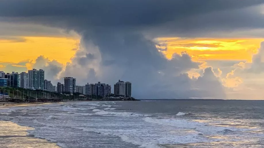 View from afar of Ponta d'Areia beach at sunset, with clouds forming behind the buildings. 