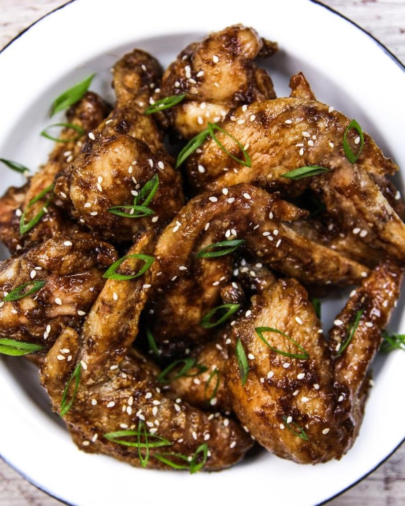 Pieces of chicken covered with dark sauce, green onions and sesame seeds close up