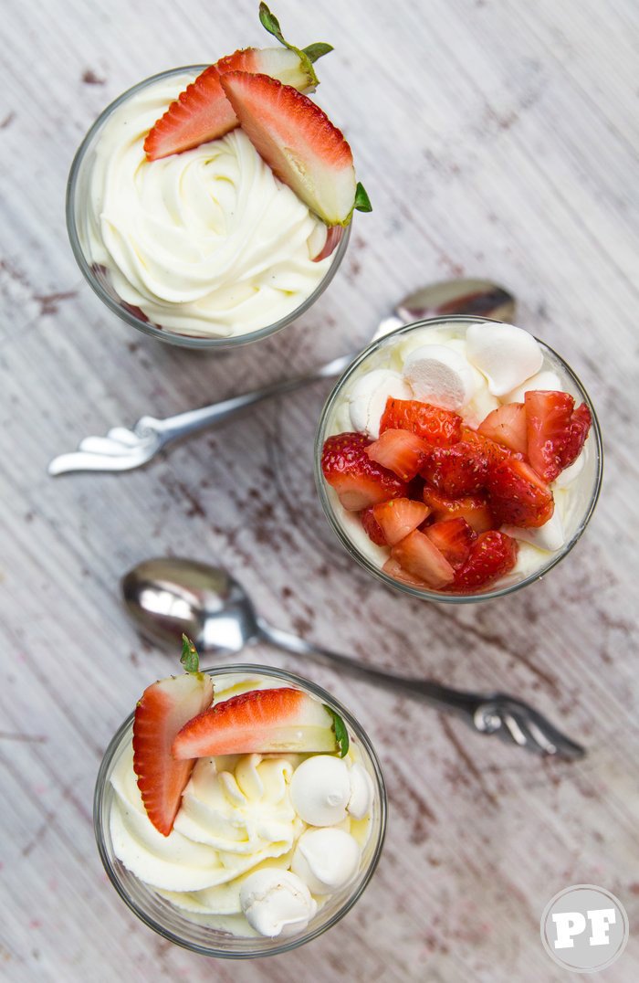 Glass with whipped cream, meringue and strawberry on white table seen from above in detail