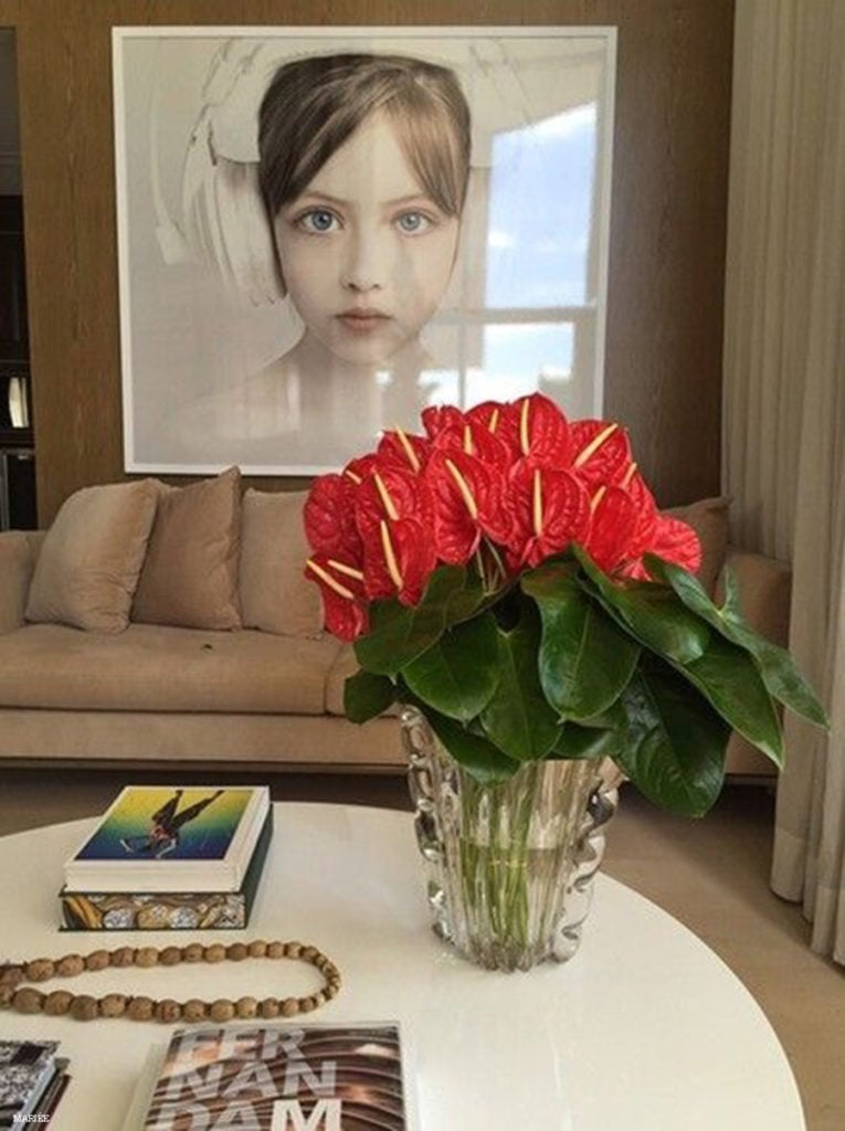 Anthurium vase on a white coffee table with book decorations, in front of a beige sofa with a painting of a girl with white headphones on top.