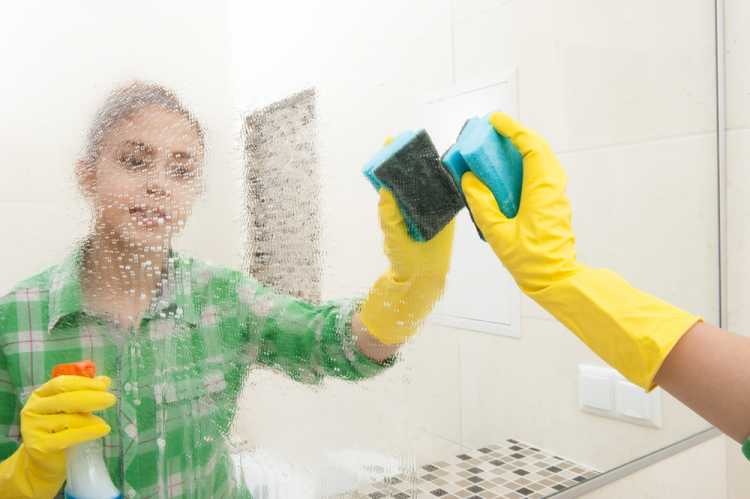 Young man using gloves to clean bathroom mirror