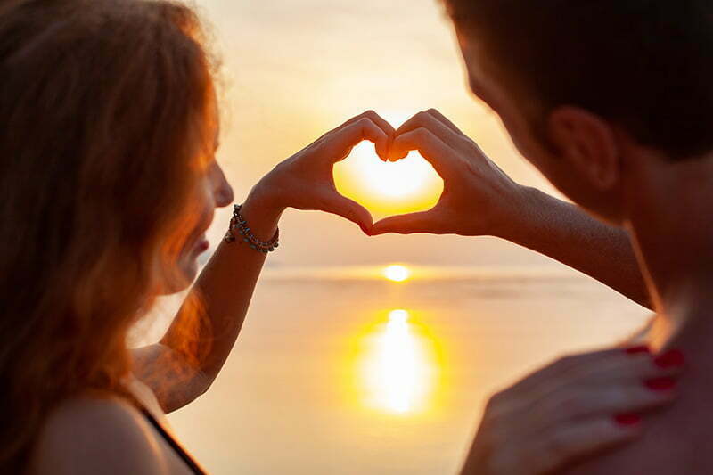 romantic couple making a heart with their hands at sunset