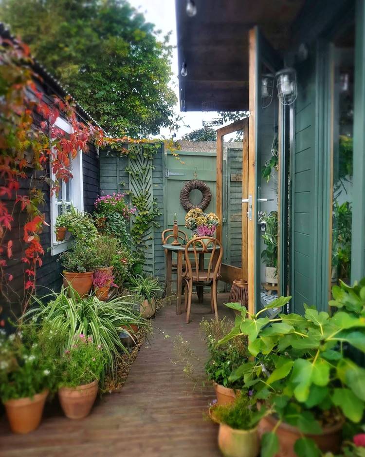 área externa de casa decorada com muitas plantas e mesa de madeira simples com flores em cima