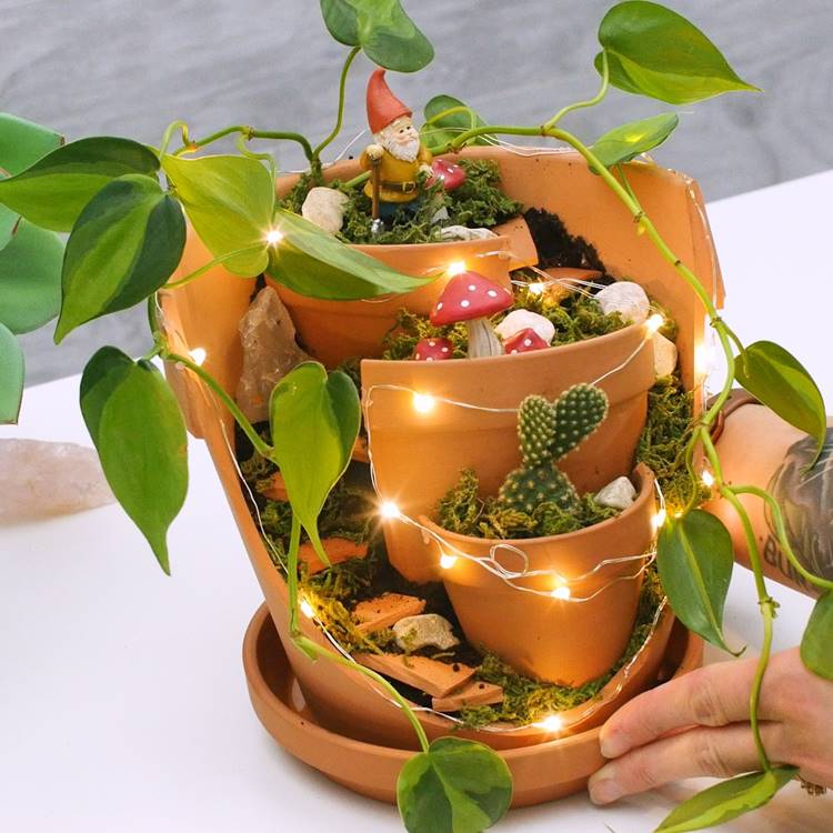 Vaso quebrado composto com jiboia, cacto e itens de decoração como anões e cogumelos.