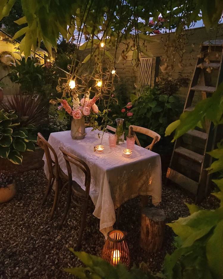 Jardim com mesa, escada velha e itens decorativos.