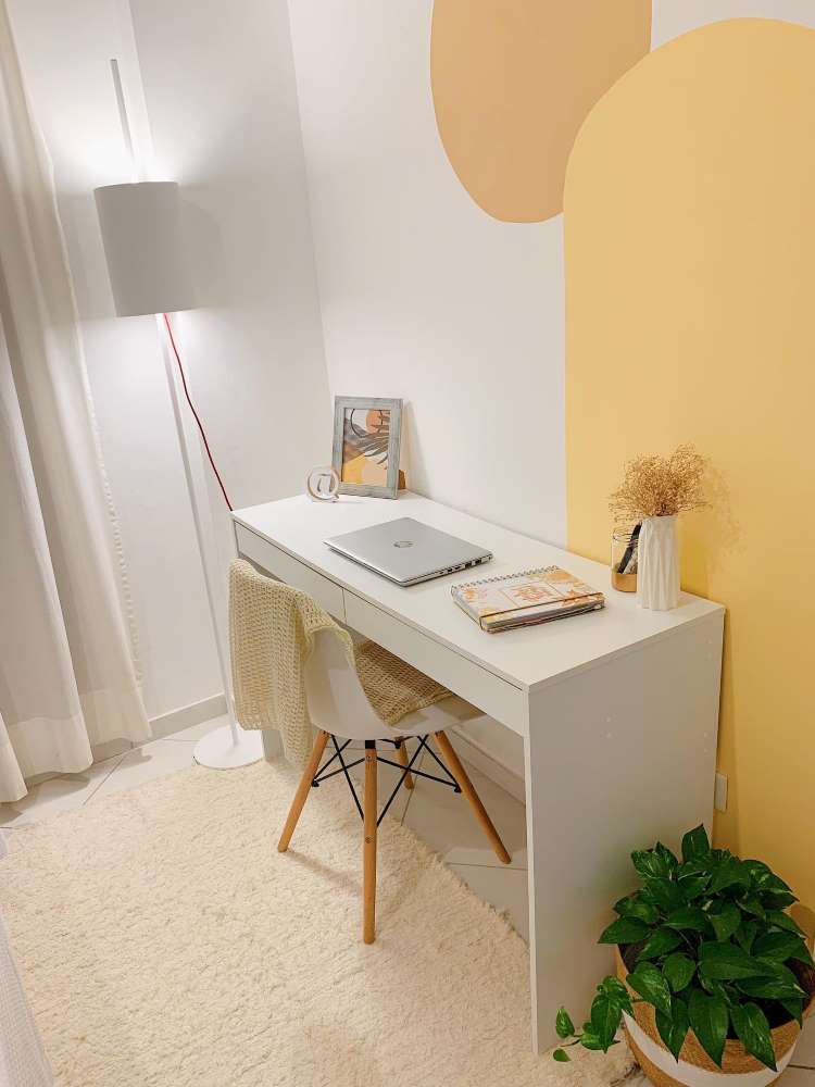 Home office in shades of white and orange, with white table, computer, rug and basket with boa constrictor. 