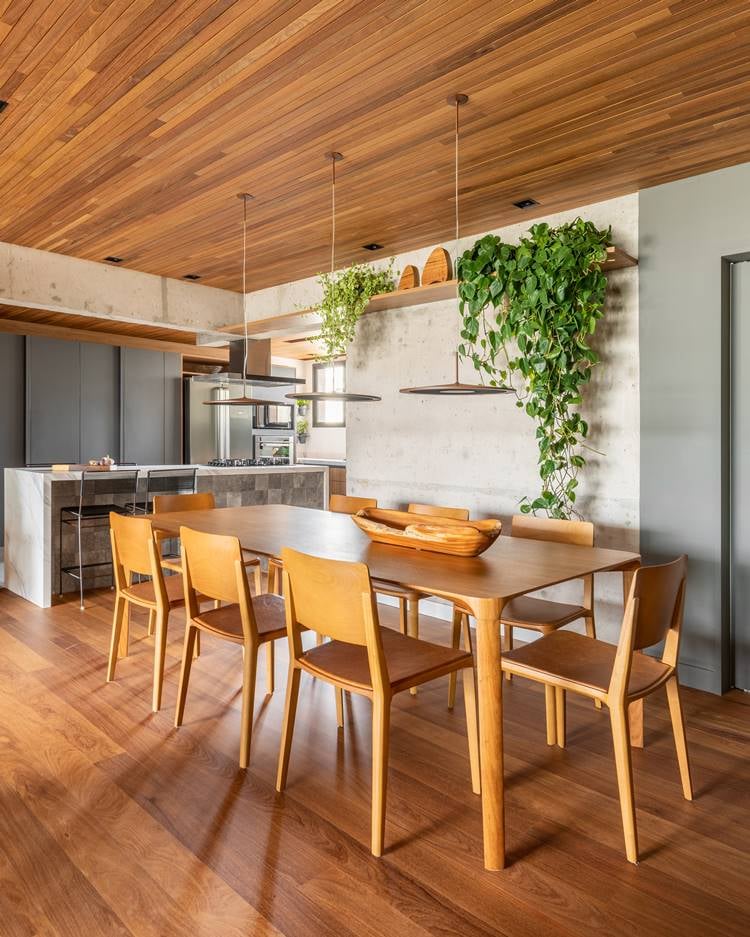 Apartment dining room measuring 187 m² decorated by architect Pietro Terlizzi, with a table with 8 wooden chairs, a shelf with a boa constrictor plant, and 3 pendant lights in the center, integrated with the kitchen