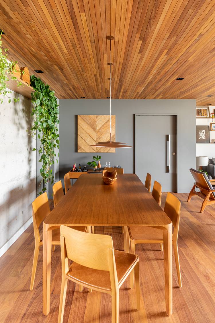 Apartment dining room measuring 187 m² decorated by architect Pietro Terlizzi, with a table with 8 wooden chairs, a shelf with a boa constrictor plant, and 3 pendant lights in the center, in the corner a mobile bar, integrated with the living room