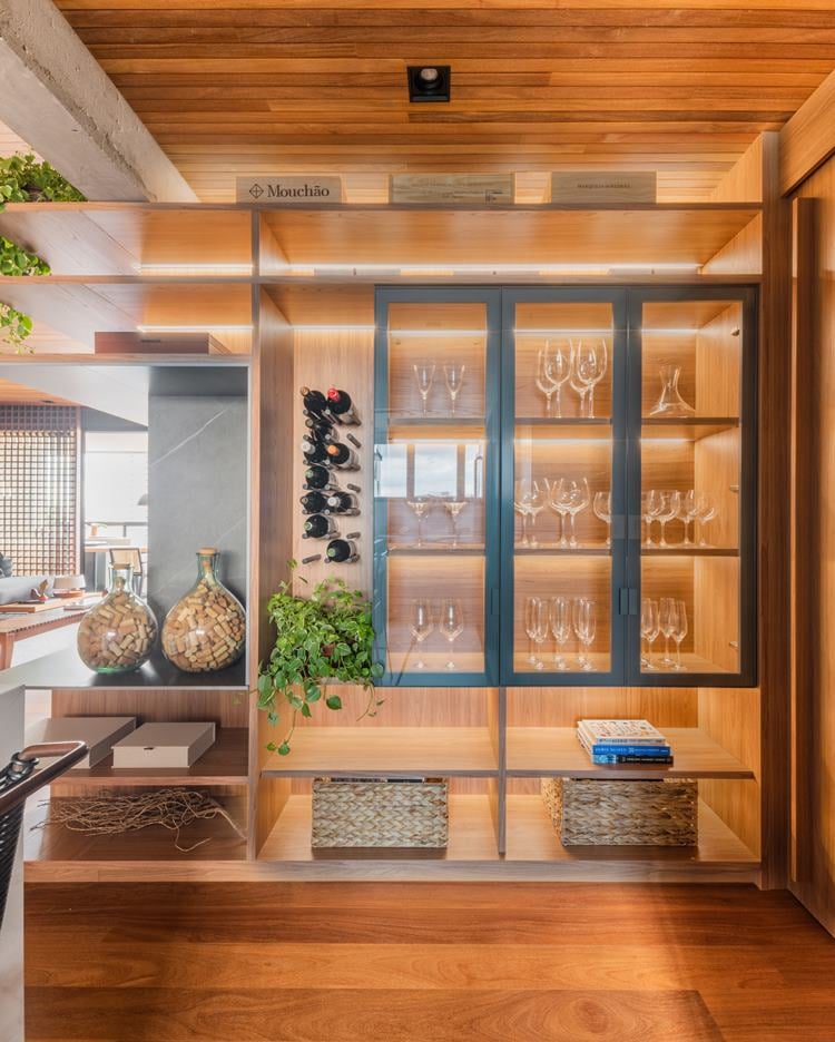 Glass cabinet in the 187 m² apartment kitchen decorated by architect Pietro Terlizzi, with glasses, alongside pins that hold drinks bottles.  Straw boxes, glass jars with corks, and MDF boxes in the external compartments of the china cabinet furniture