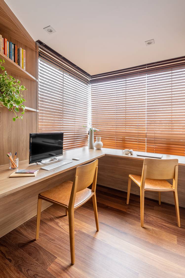 Apartment office or home office.  L-shaped table in the corner with blinds.  Two wooden chairs, computer, notebooks, notebook, headphones and other objects.