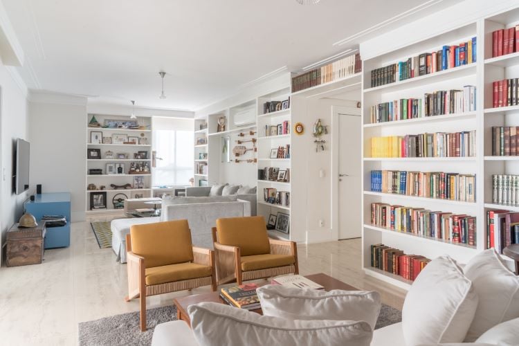 Decoration of an integrated living room environment with television and reading corner with a shelf full of books, with brown armchairs and an off-white sofa, which contributes to mental health