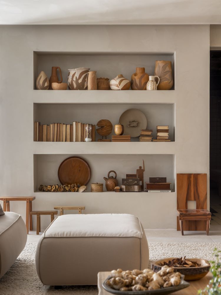 Decorating a living room shelf in neutral tones, with a puff and various ceramic vases and decorative items in earthy tones, which contributes to mental health.