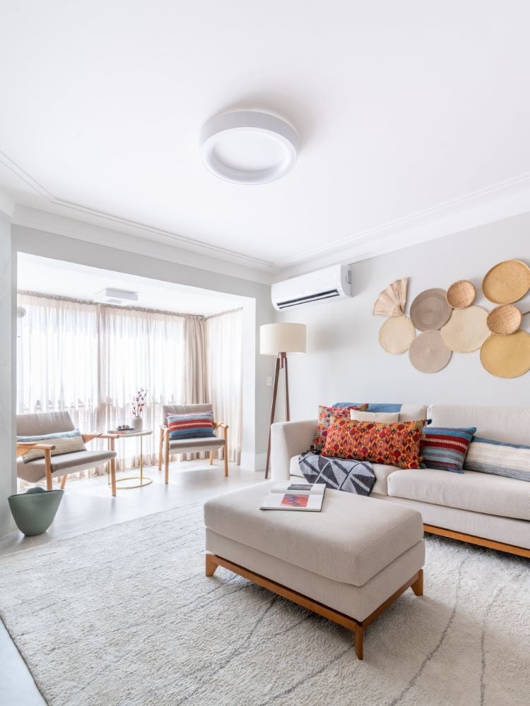 Living room with neutral colors, circular decorations in earthy tones on the wall and a huge balcony door covered by a thin curtain.