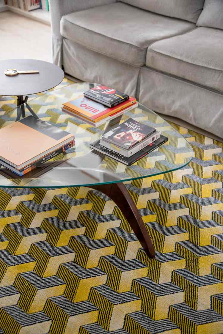 triangular glass living room coffee table, books on top and patterned rug below