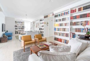 sala de estar branca ampla com poltronas e estante grande branca com muitos livros