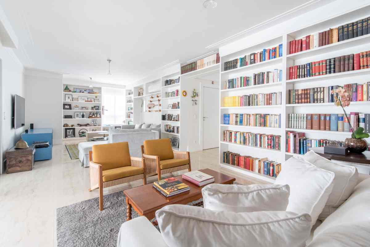 sala de estar branca ampla com poltronas e estante grande branca com muitos livros