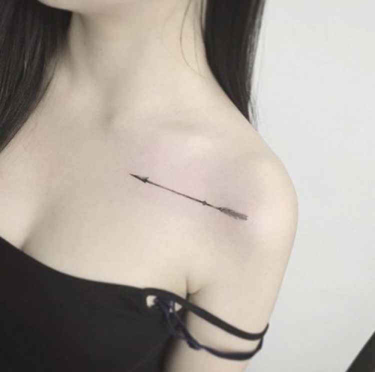 Delicate feminine tattoo on the chest at shoulder level with an arrow design