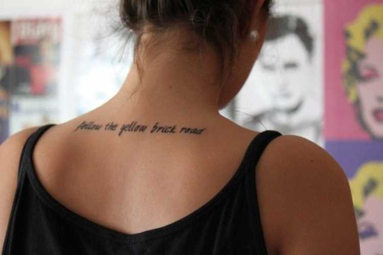 Female tattoo with sayings on the upper back