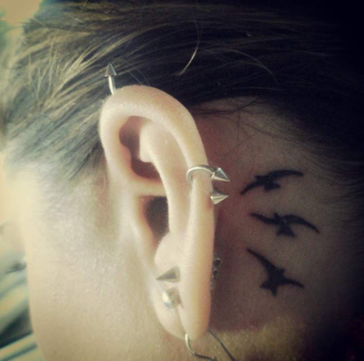 Tattoo of birds flying behind the ear