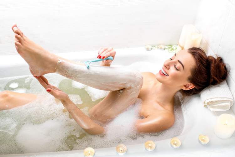 woman waxing with a razor in the bathtub