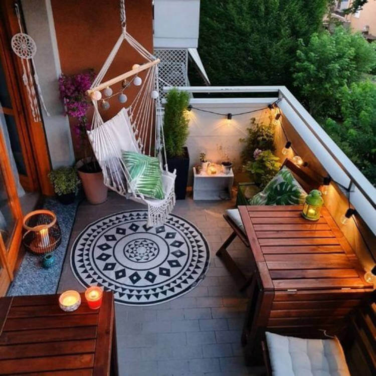 Balcony decorated with plants, pillows and swing.