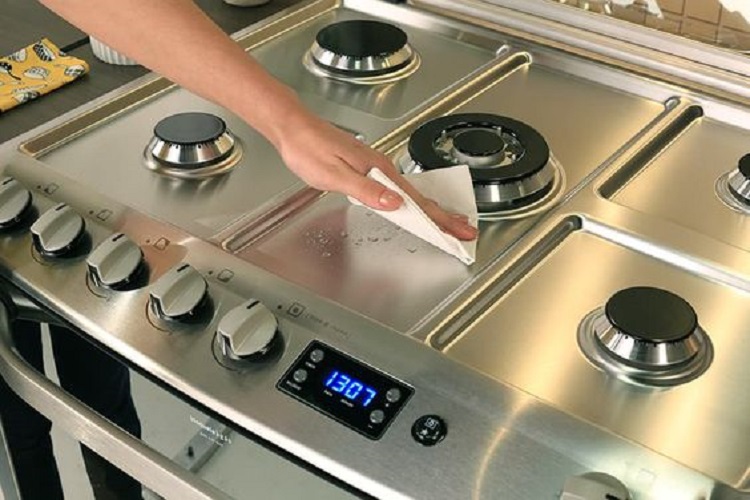 Woman cleaning a stainless steel stove.