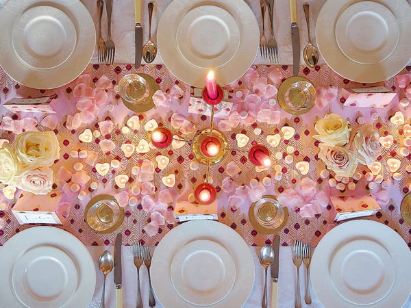 Romantic dinner table set with candlelight, rose petals and hearts spread across the table