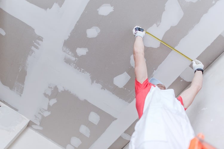 man measuring drywall ceiling