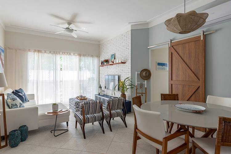 Integrated dining and living room with wooden sliding door, armchairs, white sofa, dining table, exposed brick, and decorative items. 