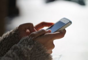 mulher usando blusa de lã e segurando celular enquanto navega por link do WhatsApp em páginas do Instagram de decoração