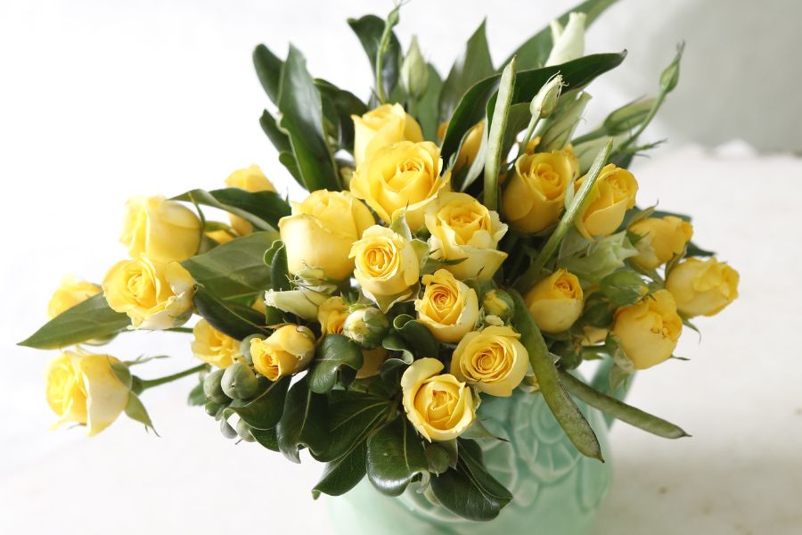 arrangement of yellow roses with foliage in a turquoise ceramic vase