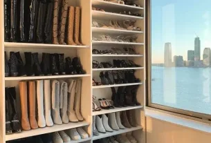 Closet com janela com vista para um grande rio com prédios ao fundo. A sapateira está repleta de tênis, botas, saltos e coturnos.