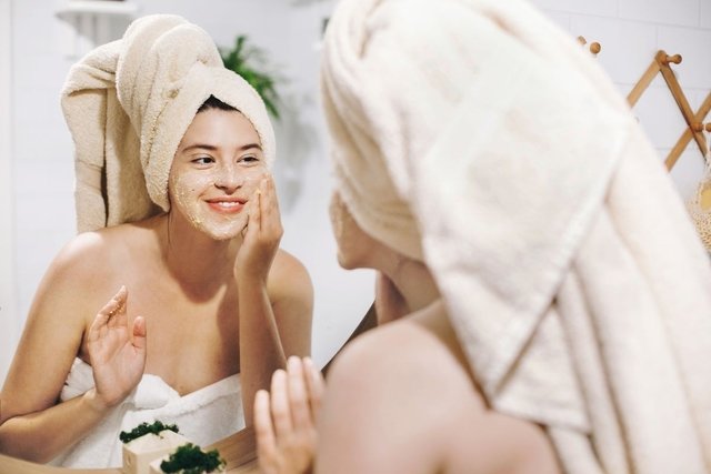 Woman looking in the mirror while applying exfoliation to her face