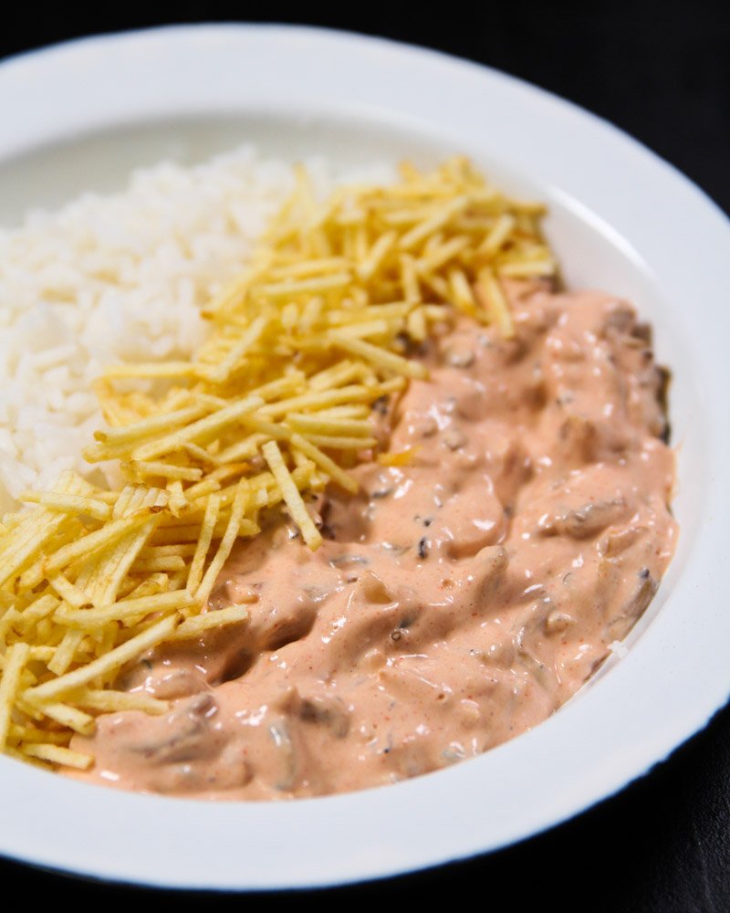 Piatto a base di riso, patate paglia e funghi alla Stroganoff su un tavolo visto da vicino.