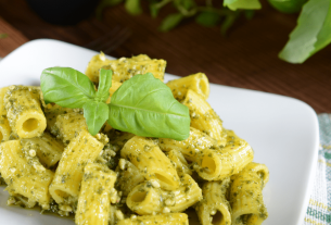 Pasta al pesto servita su un piatto bianco con contorno di basilico