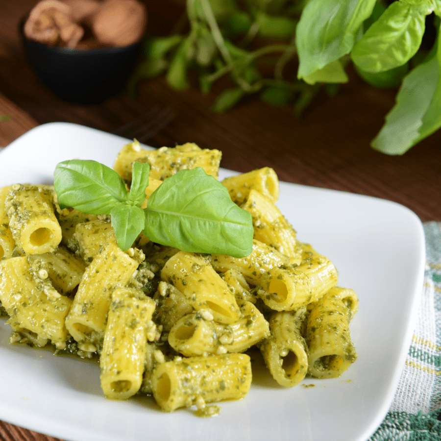 Pasta al pesto servita su un piatto bianco con contorno di basilico