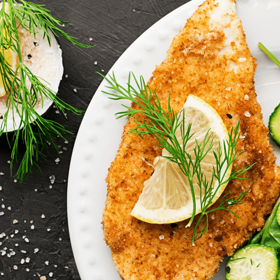 Immagine ravvicinata di pollo impanato su un piatto bianco con contorno di aneto e limone