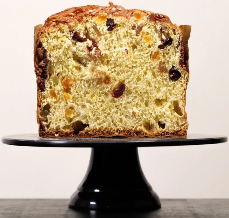 Panetone tradicional de frutas cortado ao meio mostrando o miolo sobre um pedestal.