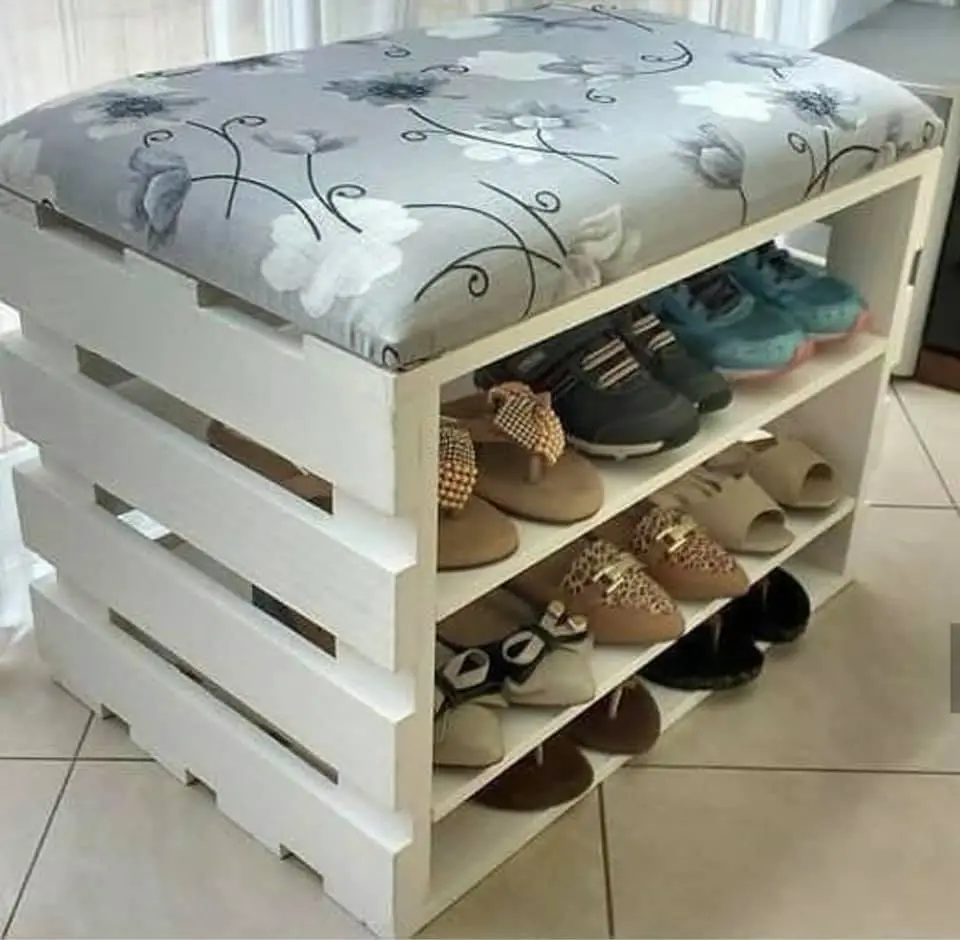 Les chaussures sont rangés dans un meuble avec deux étagères, un bois avec un coussin-gris avec une fleur sur le dessus de la table. 