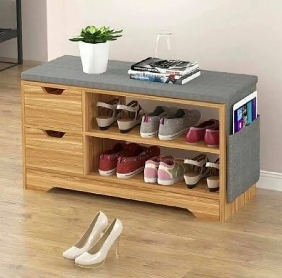 Banc en bois avec tiroirs de rangement et d'espace pour une chaussure rack. Au sommet il y a un coussin en gris, avec un pot et un magazine sur le dessus de cela. En fin de compte, il ya un stand pour un ordinateur tablette. 