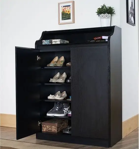 Cabinet noir transformé en une chaussure rack. La partie supérieure est utilisée comme support pour les éléments décoratifs, tels que des boîtes, des livres et des peintures. Le mobilier est placé à côté d'une image d'une fleur et d'autres de la Tour Eiffel. 