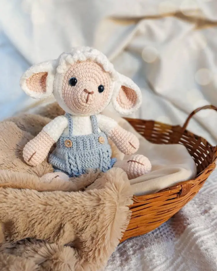 Little lamb crochet white outfit with blue, placed in a basket, adorned with a fabric, and more fabric at the bottom.