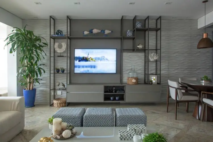 The living room in shades of grey with the shelves hollow in some parts, and closed at the other. It holds a tv, and various decorative items. 